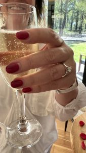 celebrating woman wearing custom engagement ring with wine of glass